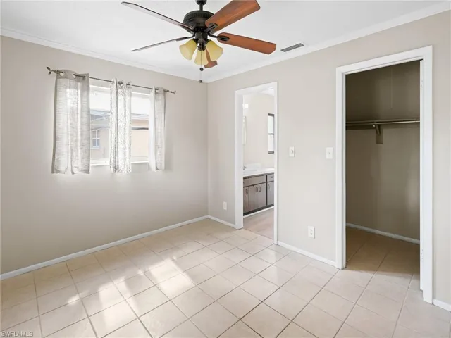 Unfurnished bedroom with crown molding, light tile patterned floors, a spacious closet, ceiling fan, and connected bathroom