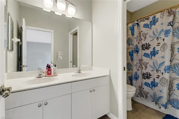 Bathroom with toilet, a shower with curtain, vanity, and tile patterned floors