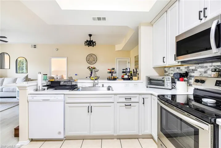 Kitchen with stainless steel appliances, open floor plan, white cabinets, and light countertops
