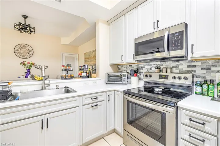 Kitchen featuring stainless steel appliances, white cabinets, light countertops, light tile patterned flooring, and tasteful backsplash