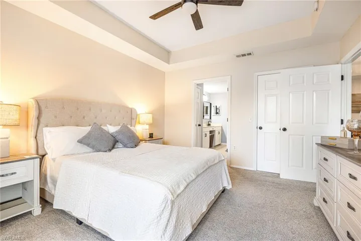 Bedroom with a raised ceiling, light carpet, connected bathroom, and ceiling fan