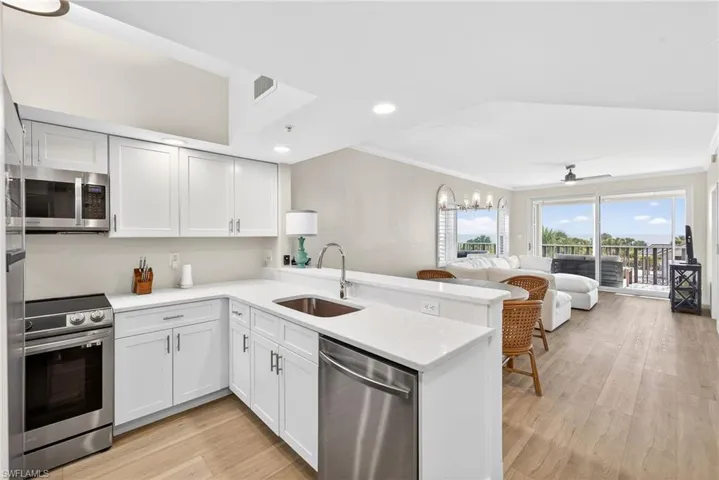 Kitchen featuring a peninsula, stainless steel appliances, open floor plan, crown molding, and light wood finished floors