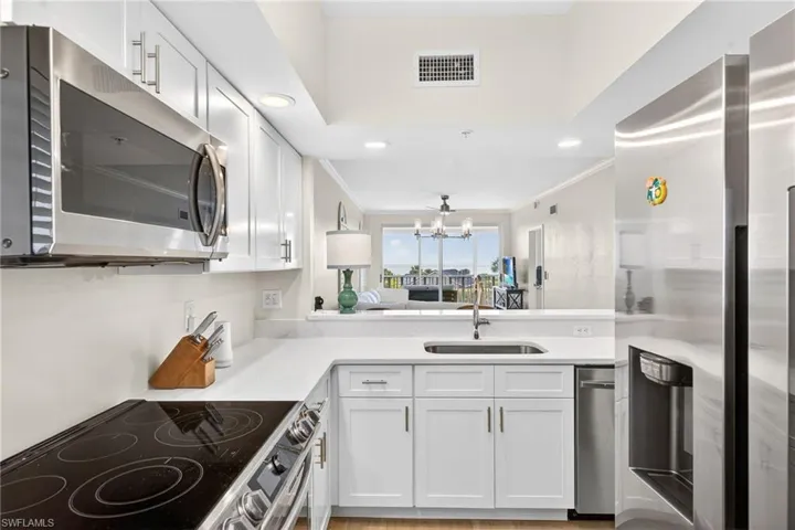 Kitchen with stainless steel appliances, crown molding, white cabinetry, and suspended lighting