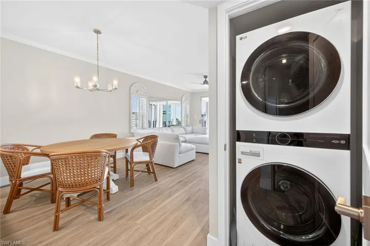 Laundry area with ornamental molding, light wood-type flooring, stacked washer / dryer, a chandelier, and a ceiling fan