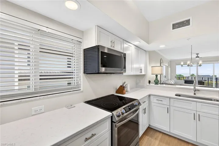 Kitchen with stainless steel appliances, white cabinetry, suspended lighting, light stone countertops, and crown molding