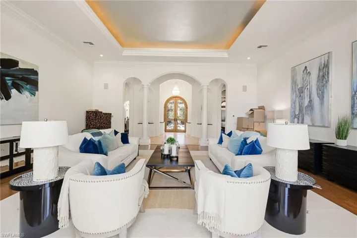 Living room featuring wood finished floors, ornamental molding, a raised ceiling, arched walkways, and recessed lighting