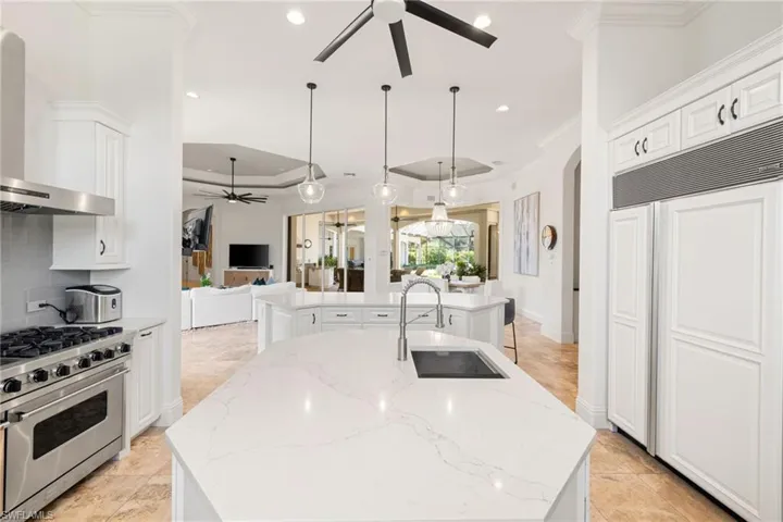 Kitchen featuring a ceiling fan, high quality appliances, light stone countertops, wall chimney range hood, and white cabinets