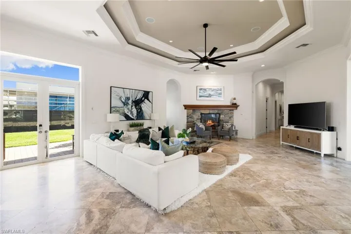Living area with ornamental molding, a fireplace, a raised ceiling, a ceiling fan, and arched walkways