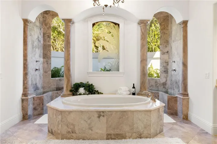 Full bath featuring decorative columns, a garden tub, and a marble finish shower