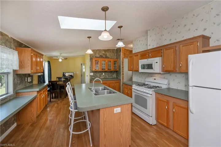 Kitchen featuring light wood-type flooring, sink, an island with sink, white appliances, and a skylight