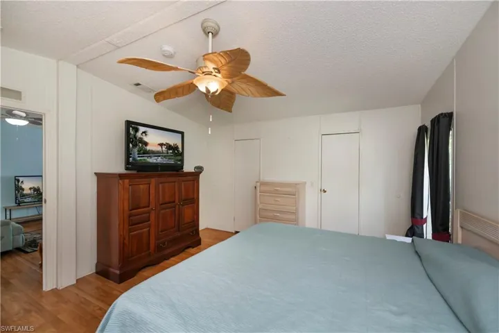 Bedroom featuring ceiling fan, hardwood / wood-style flooring, lofted ceiling, and a textured ceiling