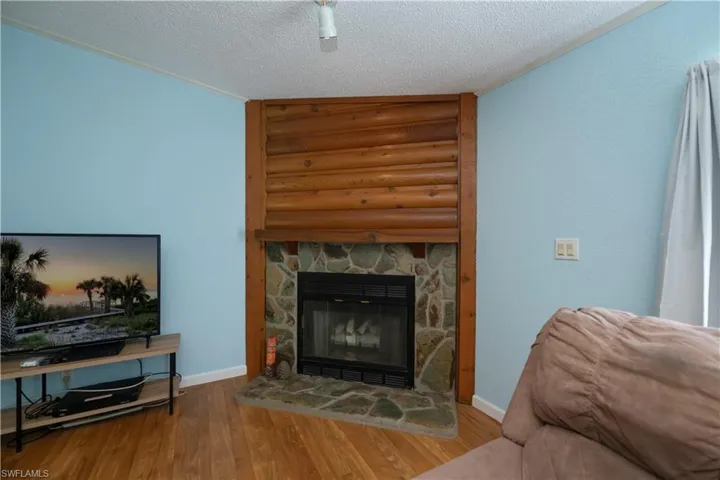 Living room with ornamental molding, wood-type flooring, a textured ceiling, and a stone fireplace