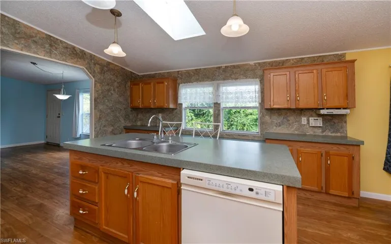 Kitchen with sink, a skylight, a center island with sink, dark hardwood / wood-style flooring, and white dishwasher