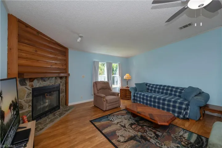 Living room featuring ceiling fan, a stone fireplace, a textured ceiling, and hardwood / wood-style floors