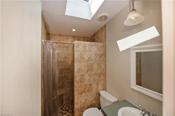 Bathroom featuring a shower with curtain, a skylight, sink, and toilet