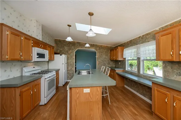 Kitchen with pendant lighting, light wood-type flooring, sink, white appliances, and a center island with sink