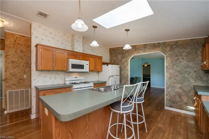 Kitchen featuring a skylight, an island with sink, sink, white appliances, and dark hardwood / wood-style flooring