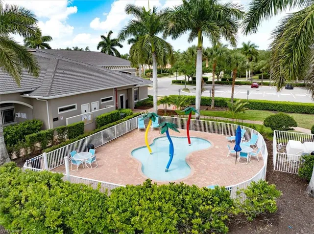 Children's splash pad with colorful palm tree water features and white picket fencing.