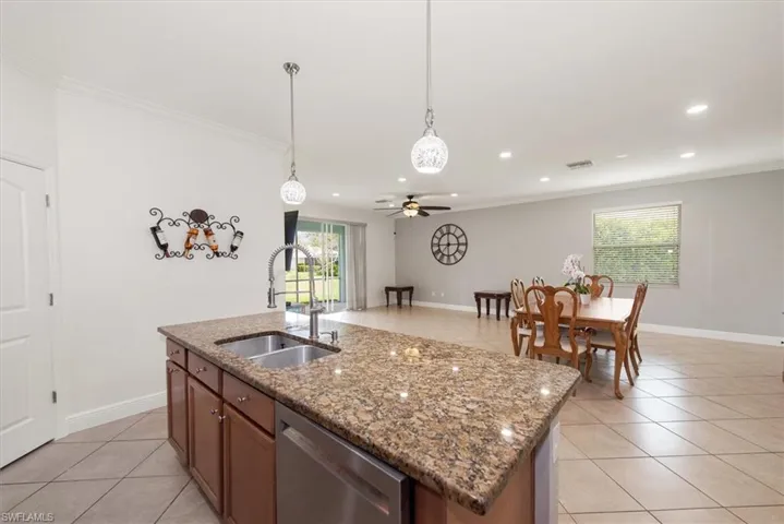 Kitchen island with granite countertops, double basin sink, dishwasher, and open area to the dining area.