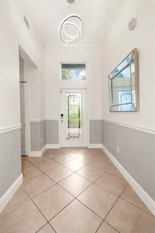 Welcoming foyer with diagonal tile flooring, modern chandelier, two-tone wall finish with chair railing, wall mirror, and glass panel entry door.