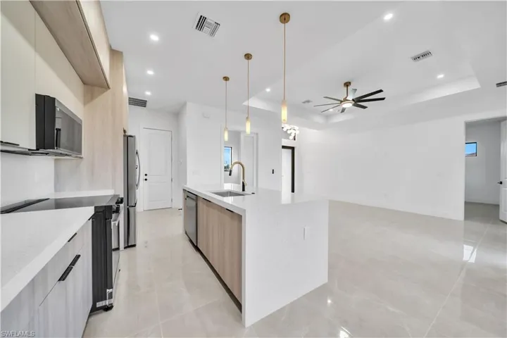 Dual tone kitchen featuring stainless steel appliances, two tone cabinets, light stone countertops, decorative light fixtures, and modern cabinets
