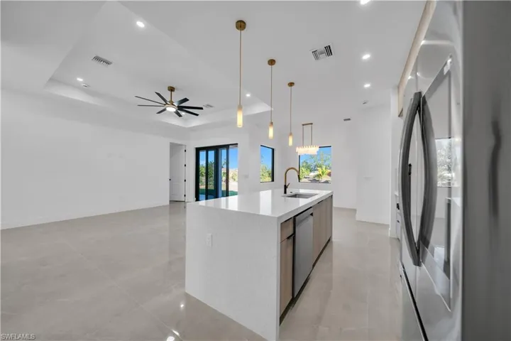 Kitchen featuring stainless steel appliances, light stone counters, hanging light fixtures, a center island with sink, and a raised ceiling