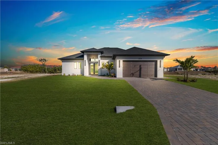 Prairie-style home with a front yard, decorative driveway, stucco siding, and an attached garage