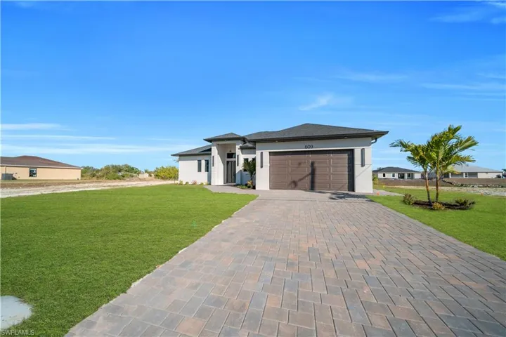 Prairie-style house with a front lawn, decorative driveway, stucco siding, and an attached garage