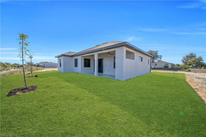 Back of property with stucco siding, a patio, a lawn, a ceiling fan, and a shingled roof