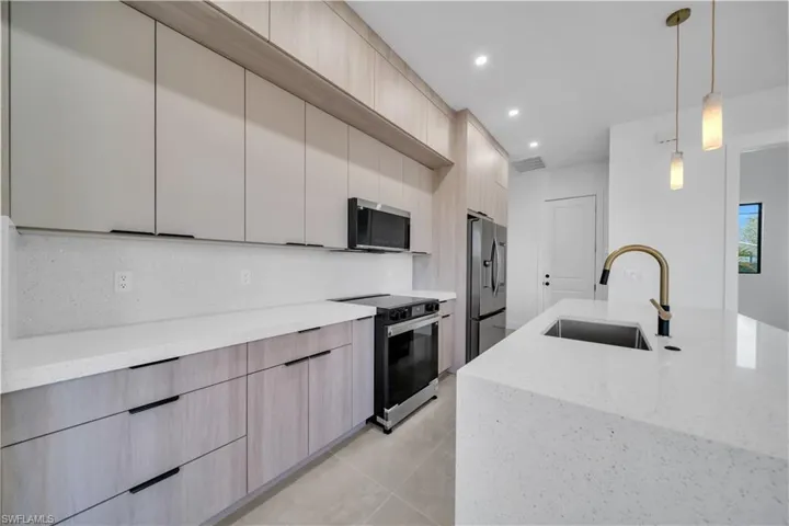 Kitchen with modern cabinets, pendant lighting, stainless steel appliances, light stone counters, and light wood finish cabinetry