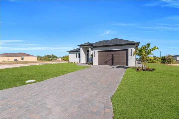 Prairie-style home featuring a front yard, decorative driveway, stucco siding, and an attached garage