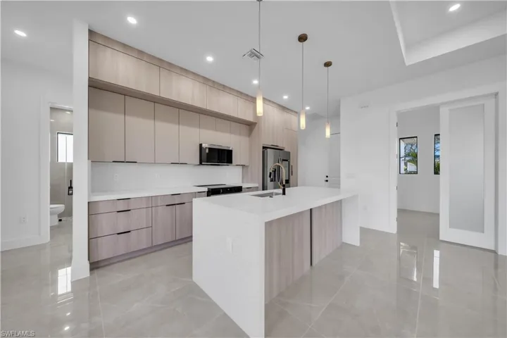 Kitchen with light wood finish cabinetry, an island with sink, and hanging light fixtures