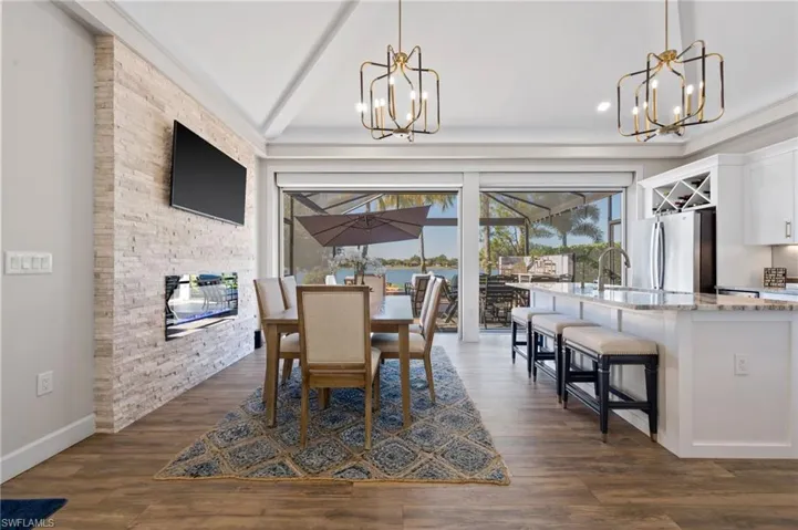 Dining room featuring dark wood-style flooring, a chandelier, a stone fireplace, a sunroom, and vaulted ceiling