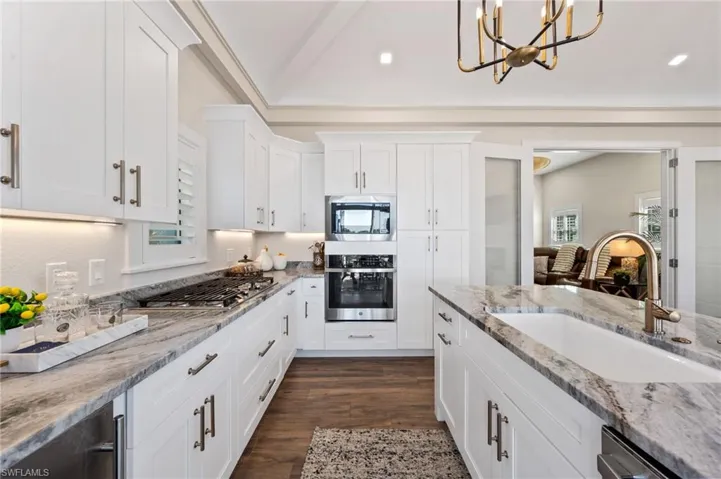 Kitchen with light stone countertops, stainless steel appliances, white cabinets, and vaulted ceiling