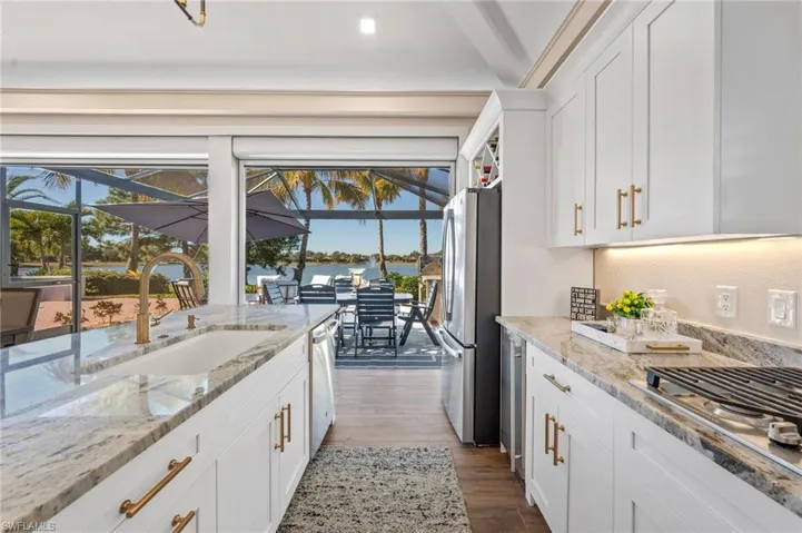 Kitchen with white cabinetry, appliances with stainless steel finishes, a sunroom, light stone counters, and dark wood-style floors