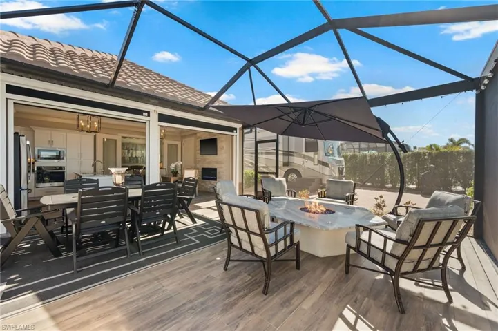 Wooden deck with outdoor dining space, a sunroom, glass enclosure, a patio area, and a fire pit