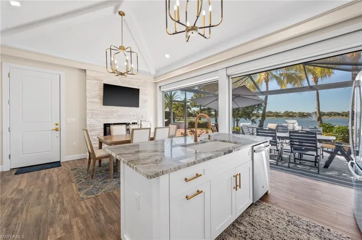 Kitchen with lofted ceiling, light stone counters, hanging light fixtures, white cabinets, and a chandelier