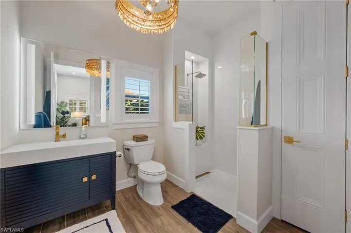 Bathroom with a walk in shower, vanity, a chandelier, and wood finished floors
