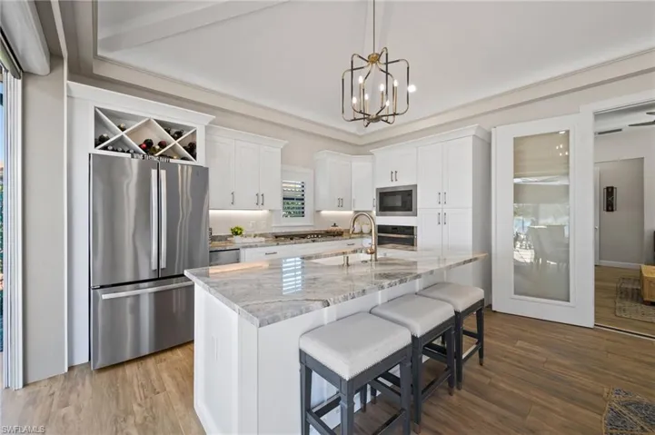 Kitchen featuring light stone countertops, appliances with stainless steel finishes, white cabinets, a kitchen bar, and a center island with sink