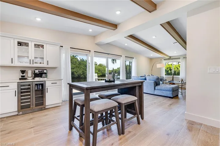 Dining space featuring recessed lighting, beverage cooler, light wood finished floors, a bar, and vaulted ceiling with beams