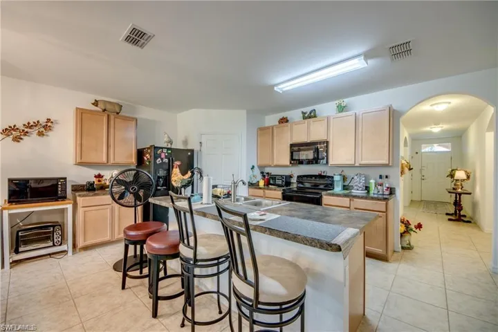 Kitchen with black appliances, a sink, light brown cabinets, and light tile patterned floors