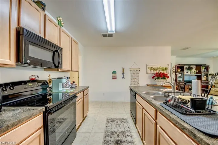 Kitchen featuring black appliances, light brown cabinetry, dark countertops, and light tile patterned floors