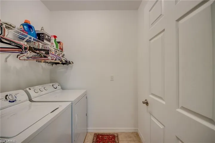 Clothes washing area with washer and clothes dryer, light tile patterned flooring, and baseboards