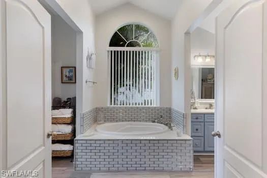 Ensuite bathroom with vanity, a bath, wood finished floors, and lofted ceiling