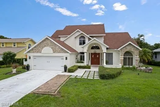 Traditional-style home featuring stone siding, driveway, a front lawn, and an attached garage