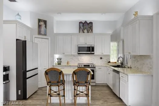 Kitchen with stainless steel appliances, white cabinets, light wood-style flooring, a breakfast bar area, and backsplash