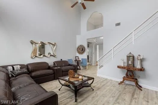 Living area featuring light wood-style flooring, ceiling fan, and a towering ceiling