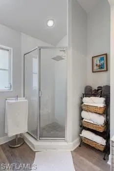 Full bathroom featuring light wood-type flooring, a shower stall, and lofted ceiling