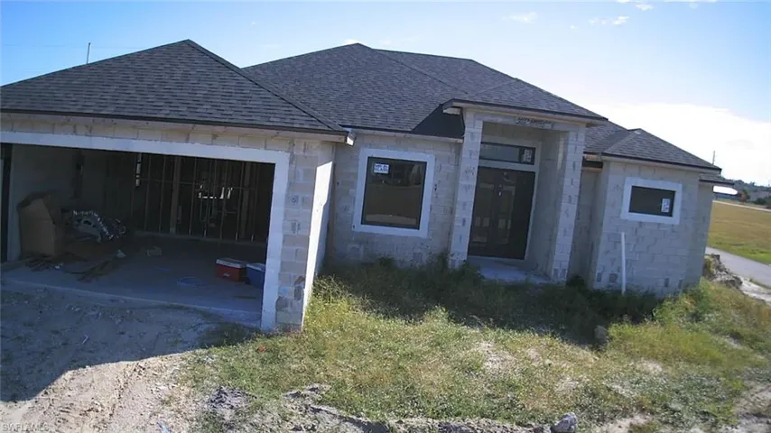 View of front of home featuring roof with shingles, an attached garage, dirt driveway, and stone siding