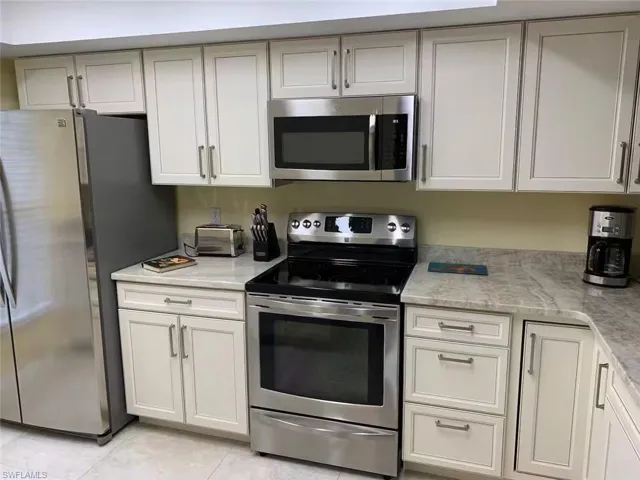 Kitchen featuring light tile patterned floors, appliances with stainless steel finishes, and light stone counters